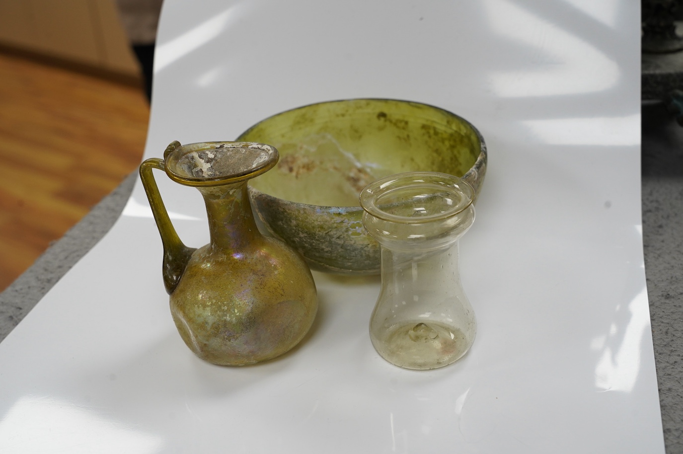 Three items of Roman glassware to include a bowl, a miniature jug and a vessel, bowl 14cm diameter. Condition - bowl repaired